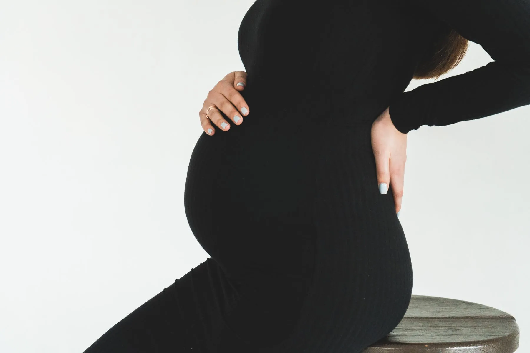 Schwangere stützt mit den Händen ihren Bauch und ihren unteren Rücken