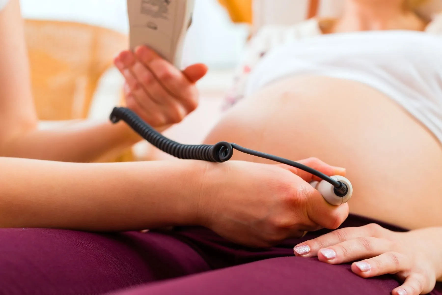 Hand hält ein Dopton-Gerät an einen Schwangerschaftsbauch, um die Herztöne des Babys zu hören